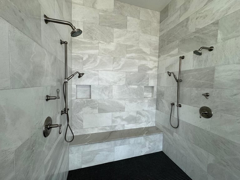 Modern spa-style bathroom shower with gray marble tile walls, dual showerheads, and black fixtures