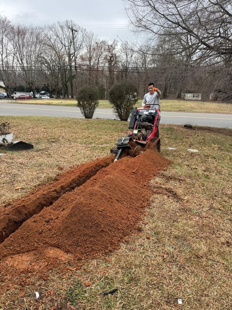 Person operating a red trenching machine digging a trench in a grassy yard